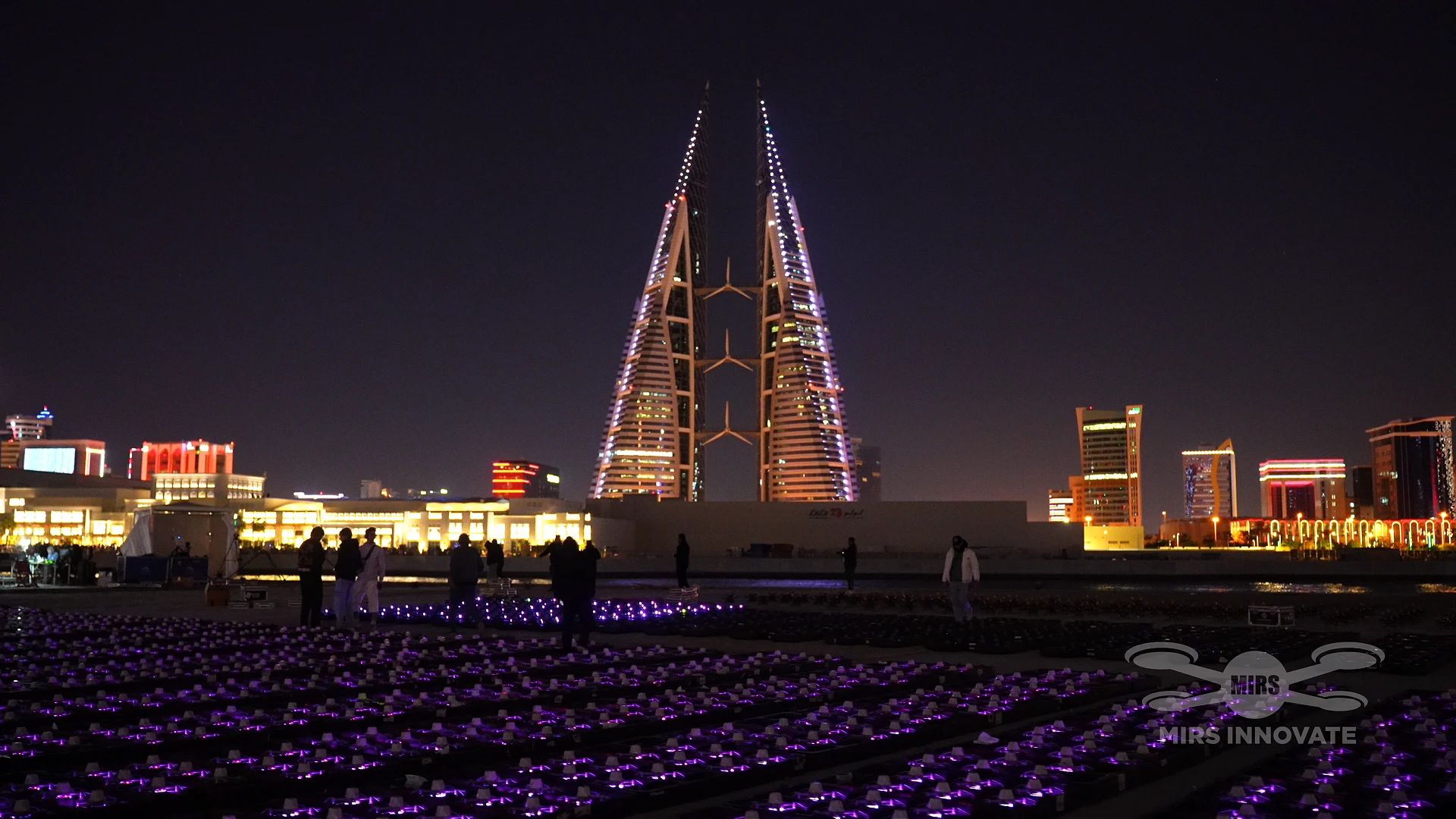 Drone fleet glowing purple on the ground in front of Bahrain World Trade Center at New Year 2026 drone show
