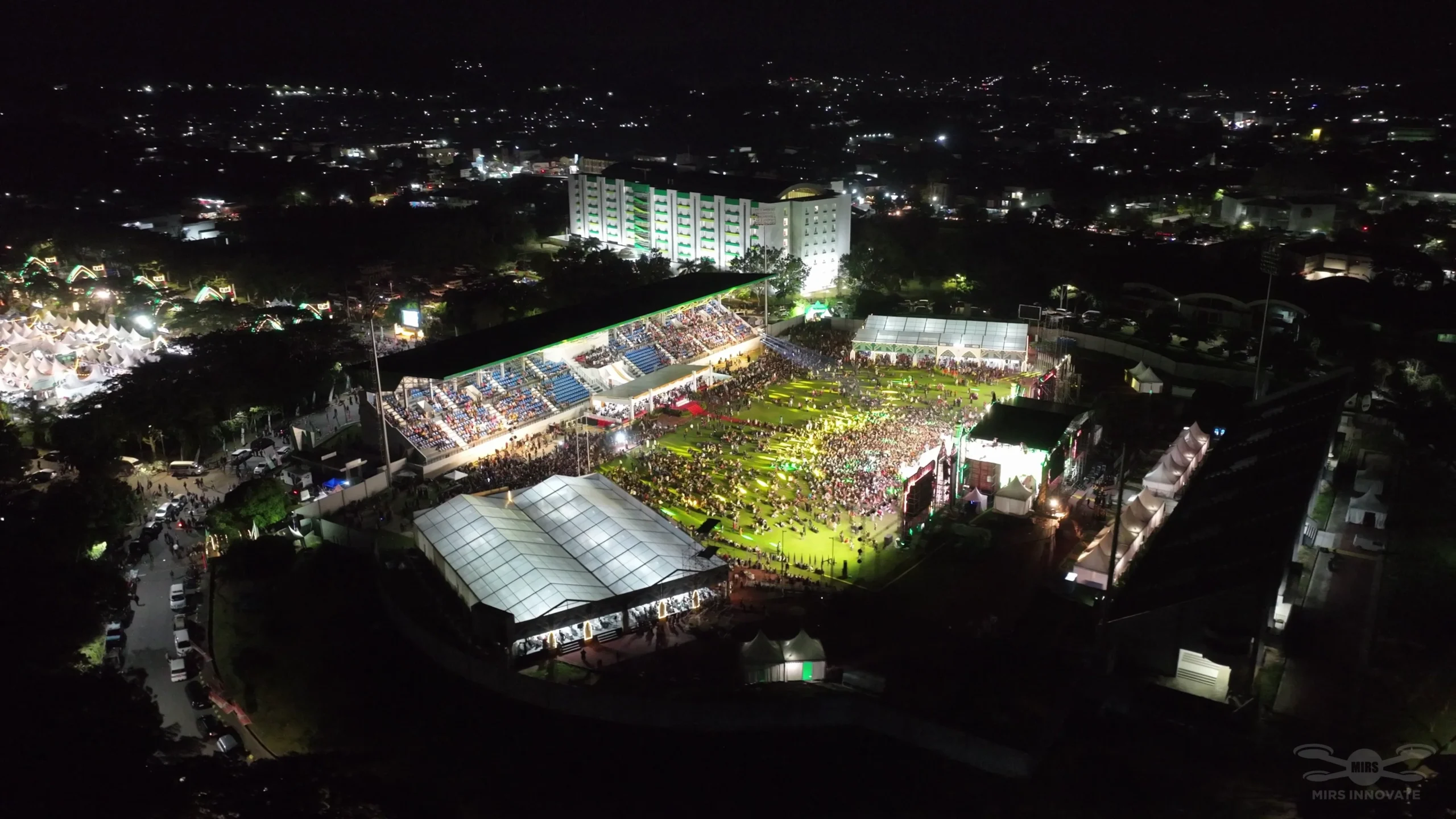 Wide night aerial view of the illuminated Samarinda Stadium venue during the MTQN XXX drone light show — 500 drones, East Kalimantan