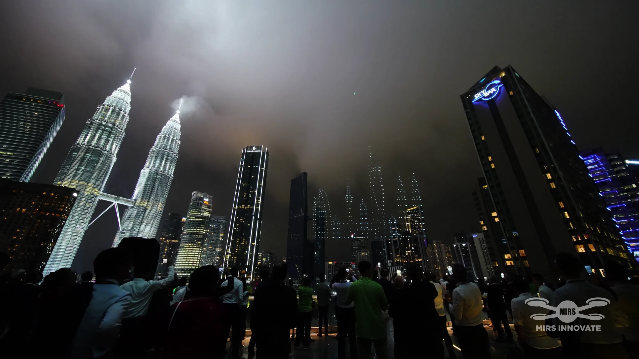 Crowd silhouette watching Deloitte drone show against Kuala Lumpur skyline and Petronas Twin Towers