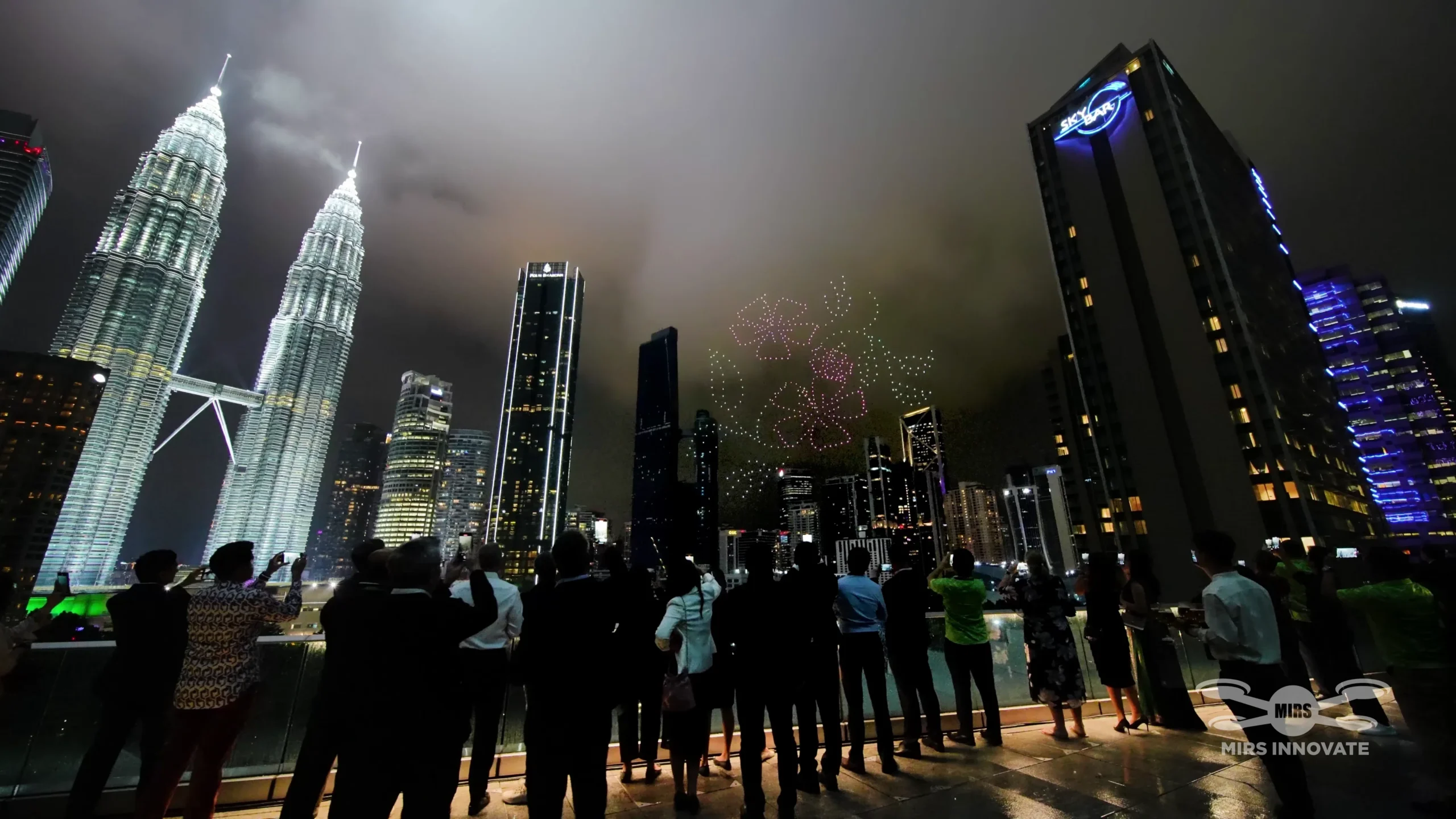 Deloitte partners crowd watching firework drone formation above Petronas Twin Towers KLCC Park