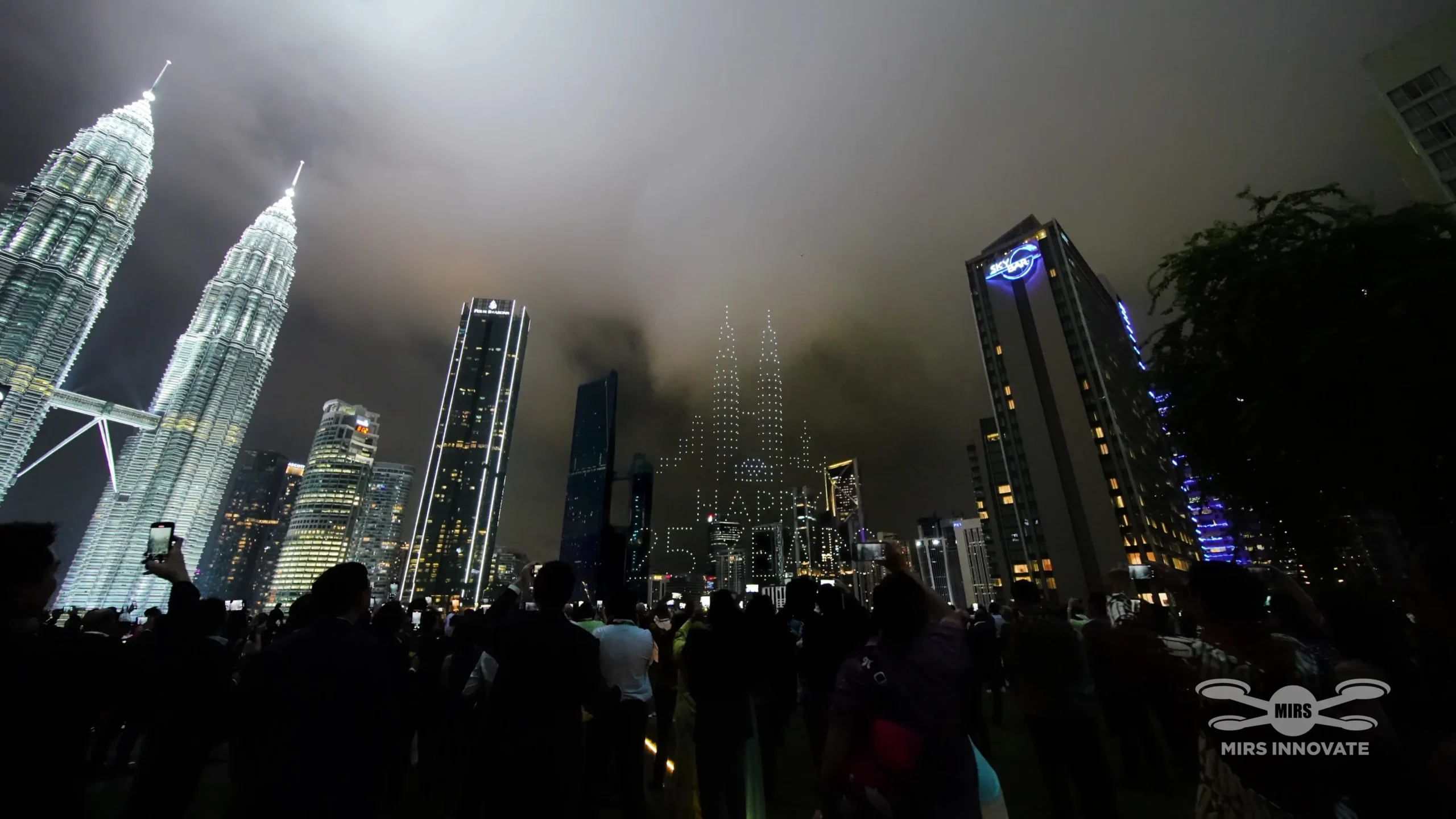 Deloitte partners crowd cheering and watching drone text formation above Petronas Twin Towers