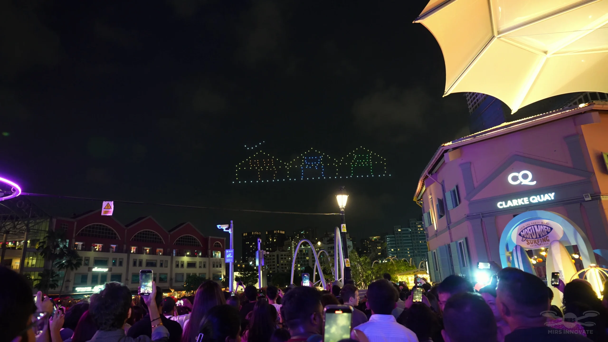 Audience watching rooftop outline drone formation at Clarke Quay Singapore