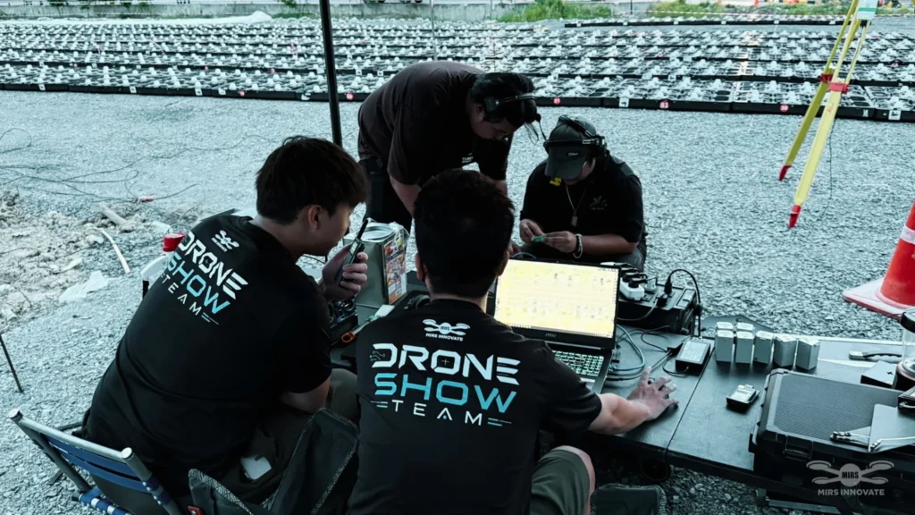 MIRS Drone Show crew reviewing flight equipment and a laptop beside a prepared drone fleet